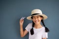 Portrait of 10s Asia black long hair pigtail girl with white hat and casual T-shirt with paper plane with blue grey wall