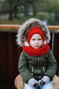 Portrait of cute sad little girl in warm outerwear clothing sitting outdoors alone Royalty Free Stock Photo