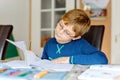 Portrait of cute school kid boy wearing glasses at home making homework. Little concentrated child writing with colorful Royalty Free Stock Photo