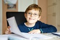 Portrait of cute school kid boy wearing glasses at home making homework. Little concentrated child writing with colorful