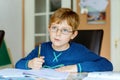 Portrait of cute school kid boy wearing glasses at home making homework. Little concentrated child writing with colorful Royalty Free Stock Photo