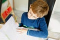 Portrait of cute school kid boy wearing glasses at home making homework. Little concentrated child writing with colorful Royalty Free Stock Photo