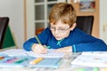 Portrait of cute school kid boy wearing glasses at home making homework. Little concentrated child writing with colorful Royalty Free Stock Photo