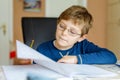 Portrait of cute school kid boy wearing glasses at home making homework. Little concentrated child writing with colorful Royalty Free Stock Photo