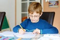 Portrait of cute school kid boy wearing glasses at home making homework. Little concentrated child writing with colorful Royalty Free Stock Photo