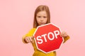 Portrait of cute serious bossy little girl holding Stop symbol, showing red traffic sign and pointing to camera Royalty Free Stock Photo