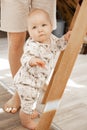 Portrait of cute serious grey-eyed plump cherubic baby infant toddler wearing beige bodysuit with patterns standing.