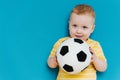 Portrait of cute shy blond little toddler boy in T-shirt holding football ball Royalty Free Stock Photo