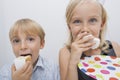 Portrait of cute siblings eating birthday cake slices in house