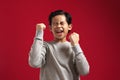 Portrait of cute smart young Asian boy wearing grey shirt shows winning gesture and smiling at camera, celebrating success victory Royalty Free Stock Photo