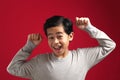 Portrait of cute smart young Asian boy wearing grey shirt shows winning gesture and smiling at camera, celebrating success victory Royalty Free Stock Photo