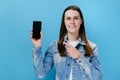 Portrait of cute smiling brunette woman pointing finger at blank screen mobile phone and happy looking at camera Royalty Free Stock Photo