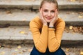 Portrait of cute smiling girl dreamily looking in camera sitting on stairs in city park