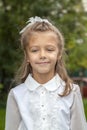 Portrait of cute smiling little caucasian girl in white blouse and bow, against green of summer park. Child go to school Royalty Free Stock Photo