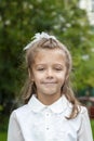 Portrait of cute smiling little caucasian girl in white blouse and bow, against green of summer park. Child go to school Royalty Free Stock Photo