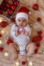 Portrait of cute smiling little girl in Santa Claus red hat on a beige plaid with Christmas decorations. Royalty Free Stock Photo