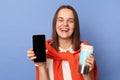 Portrait of cute smiling woman in white T-shirt and orange sweater tied over shoulders, showing empty display of her phone, Royalty Free Stock Photo