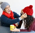 Portrait of cute smiling young adult Asian lover couple in sweatshirt, scarf, knitted hat relaxing on couch. The husband tries to