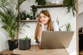 Portrait of a cute student girl sitting with a laptop in a cozy cafe with greenery, looking into the camera and smiling. Pretty Royalty Free Stock Photo