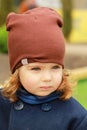 Portrait of a cute stylish serious one year old baby girl wearing a dark blue coat, scarf and a brown hat on a lovely sunny autumn Royalty Free Stock Photo