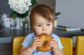 Portrait of cute thoughtful baby boy with stylish haircut holding and eating big bagel with open mouth Royalty Free Stock Photo