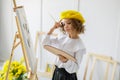 Portrait of cute thoughtful little girl artist in yellow beret who paints picture in studio while holds color pallete Royalty Free Stock Photo