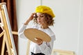 Portrait of cute thoughtful little girl artist in yellow beret who paints picture in studio while holds color pallete Royalty Free Stock Photo