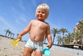 Portrait of a cute toddler boy playing with the sand at the beach in sunlight. Royalty Free Stock Photo