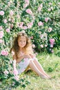 Portrait of a cute toddler girl outdoor in a rose garden sitting under the bushes