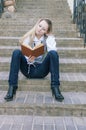 Portrait of Cute and Tranquil Caucasian Blond Woman Reading Book While Sitting Straight on Stairs Outdoors Royalty Free Stock Photo