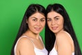 Portrait of cute twins brunettes on a green background. Posing and smiling looking at the camera.