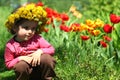 Portrait of a cute two years old girl wearing a dandelion wreath, sitting near the tulips Royalty Free Stock Photo