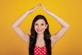 Portrait of cute woman raise hands make roof figure wear dotted red dress on yellow background