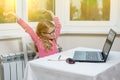 Portrait of a cute 7 year old girl wearing glasses, using a laptop, smartphone and writing in a notepad sitting at the table. Royalty Free Stock Photo