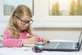 Portrait of a cute 7 year old girl wearing glasses, using a laptop, Royalty Free Stock Photo