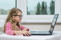 Portrait of a cute 7 year old girl wearing glasses, using a laptop, smartphone and writing in a notepad sitting at the table Royalty Free Stock Photo