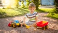 Portrait of cute 3 years old toddler boy sitting on the playground at park and playing with colorful plastic toy truck Royalty Free Stock Photo