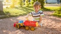 Portrait of cute 3 years old toddler boy sitting on the playground at park and playing with colorful plastic toy truck Royalty Free Stock Photo