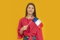 Portrait of cute young girl with the flag of France in her hands on orange background. Learn French. Immigration to France