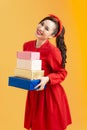 Portrait of a cute young girl in red dress holding stack of present boxes isolated over orange background Royalty Free Stock Photo