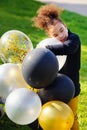 Portrait of a cute young little black girl playing with balloons in the Park. Black and gold silver balloons in the hands of a Royalty Free Stock Photo