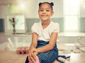 Portrait of a cute young mixed race girl sitting on the kitchen counter smiling and wearing an apron looking thoughtful Royalty Free Stock Photo