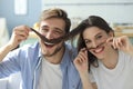 Portrait of cute young playful couple teasing with fake mustache sitting in sofa Royalty Free Stock Photo