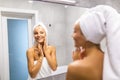 Portrait of cute young woman with towel on head, touching face reflected in mirror Royalty Free Stock Photo