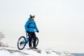 Portrait of Cyclist in Blue Resting with Mountain Bike on Rocky Winter Hill. Extreme Sport and Enduro Biking Concept.