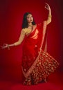 Portrait, dance and Indian woman with traditional dress, celebration and motion against a red studio background. Face