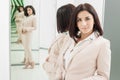 Portrait of a dark-haired attractive woman who is dressed in beige suit. standing in front mirror Royalty Free Stock Photo