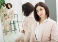 Portrait of a dark-haired attractive woman who is dressed in beige suit. standing in front mirror Royalty Free Stock Photo