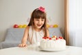 Portrait of dark haired excited happy little girl looking at birthday cake, celebrating her holiday, expressing positive emotions Royalty Free Stock Photo