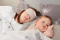 Portrait of dark haired female wearing blindfold lying with her baby in bed, daughter already wake up and looking around, mommy